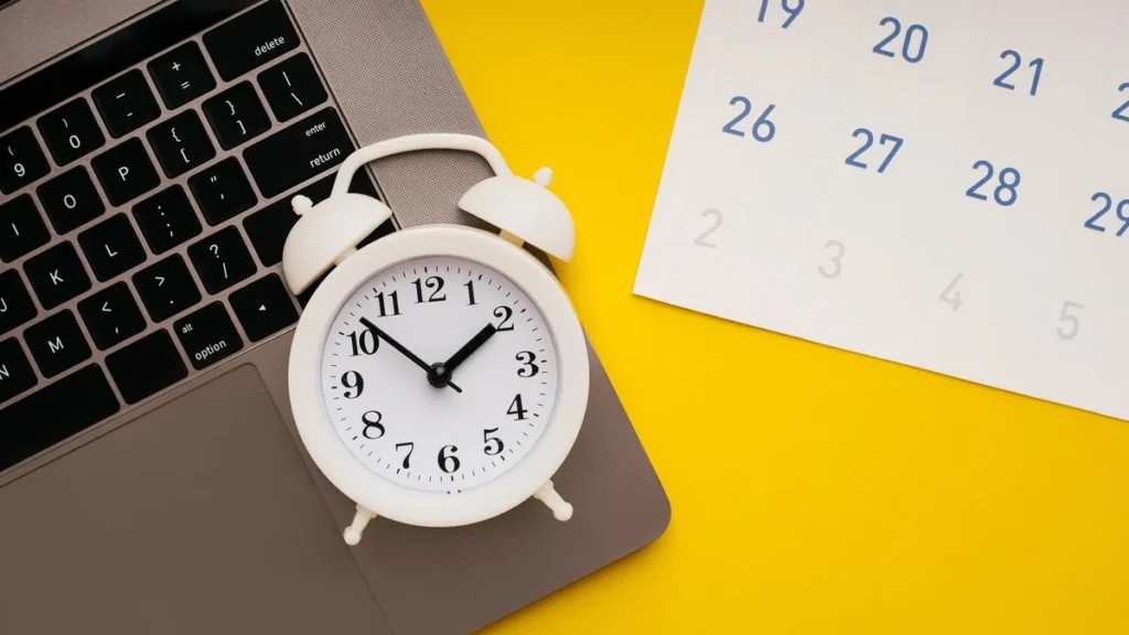 Despertador sobre notebook ao lado de um calendário